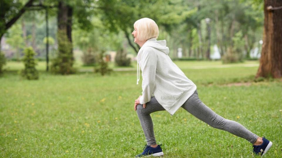 Senior sportswoman exercising and doing lunges on lawn in park