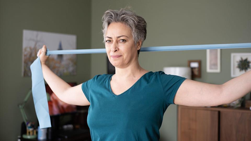  Woman stretching at home using strap. 