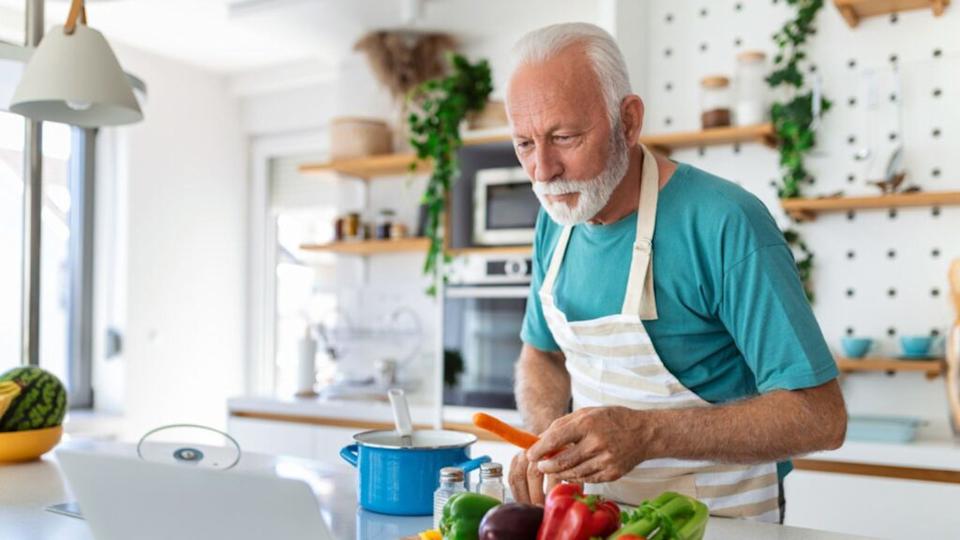 happy old man cooking soup in kitchen with vegetables