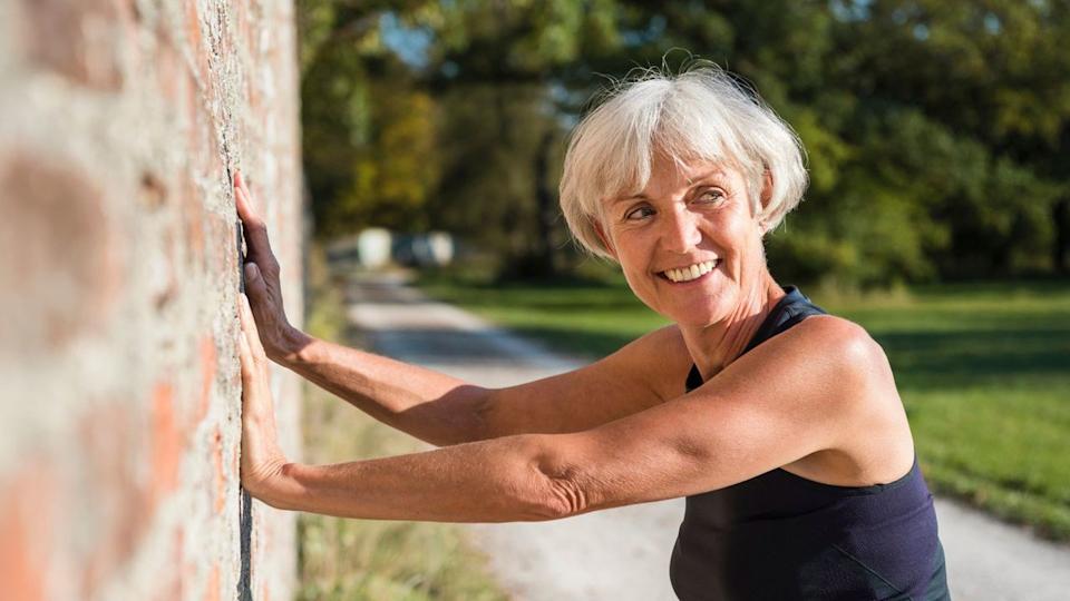 Senior woman leans against a brick wall using her hands.