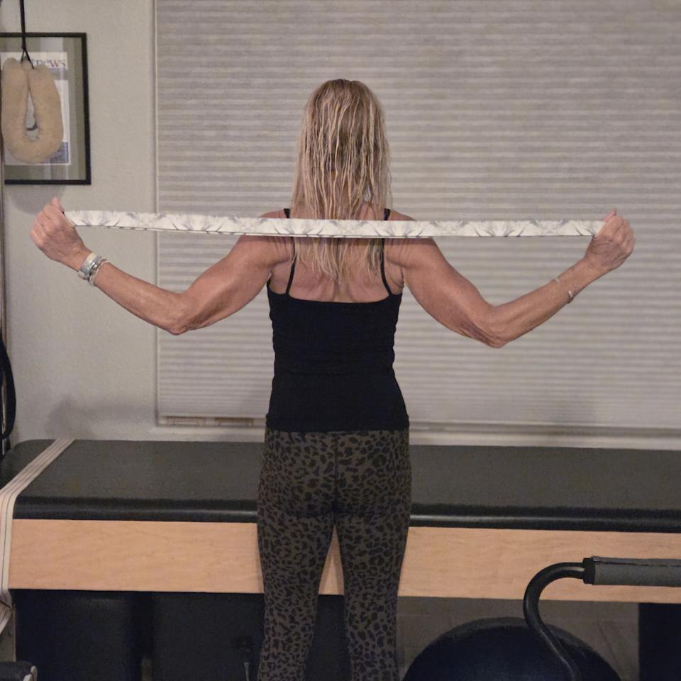 Woman stretching with yoga strap in front of a Pilates reformer bed