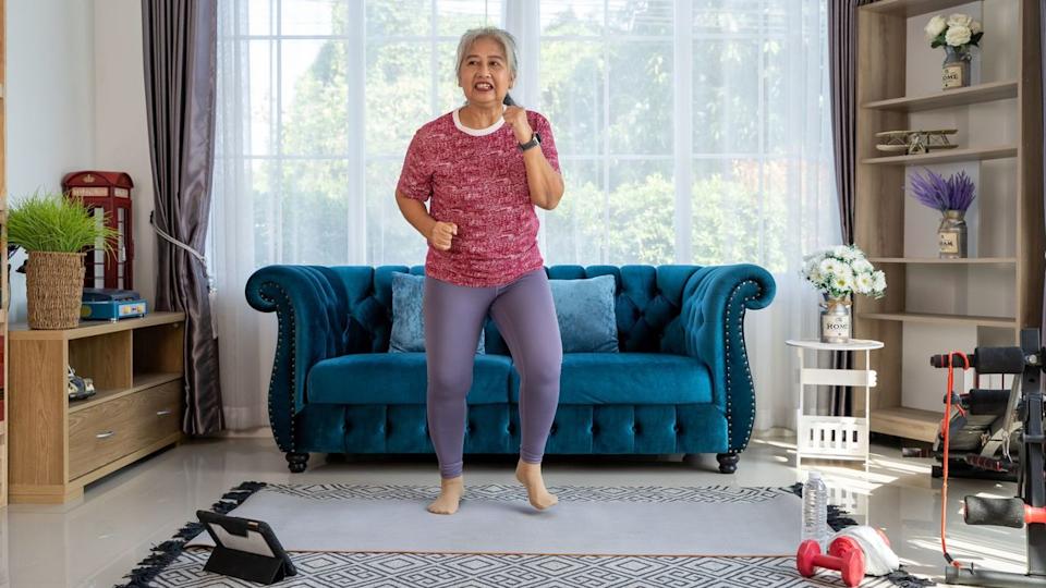  Senior woman walks on the spot doing an at-home walking workout. 