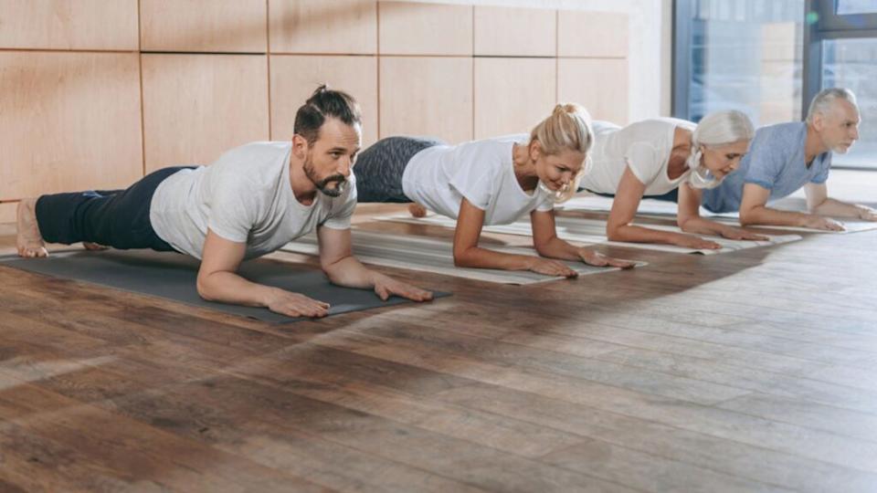 Group of people doing plank on yoga mats in studio