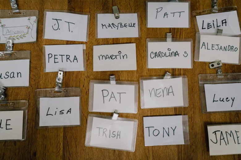Several handwritten name tags in plastic sleeves are arranged on a wooden surface, labeled with names such as Petra, Martin, Carolina, Pat, Nena, Lisa, Tony, and Leila.