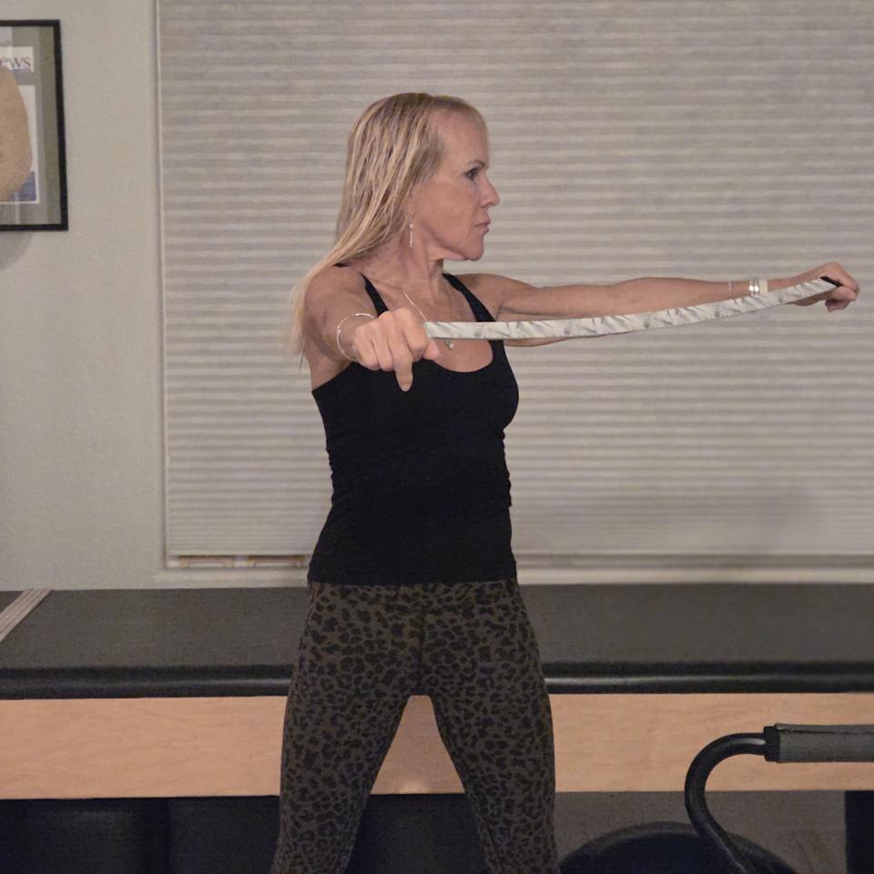 Woman stretching with yoga strap in front of a Pilates reformer bed