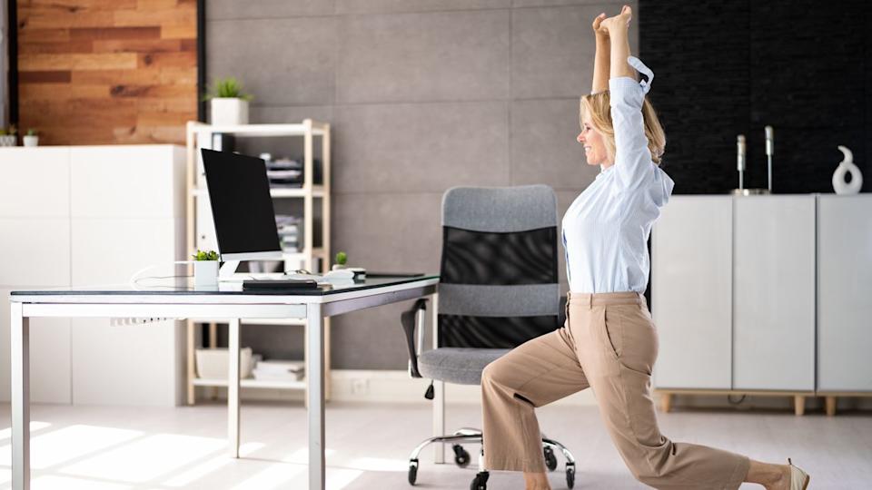  Woman in business attire stretches in front of a desk. 
