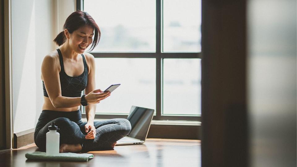 Woman looking down at phone smiling with water bottle and laptop.