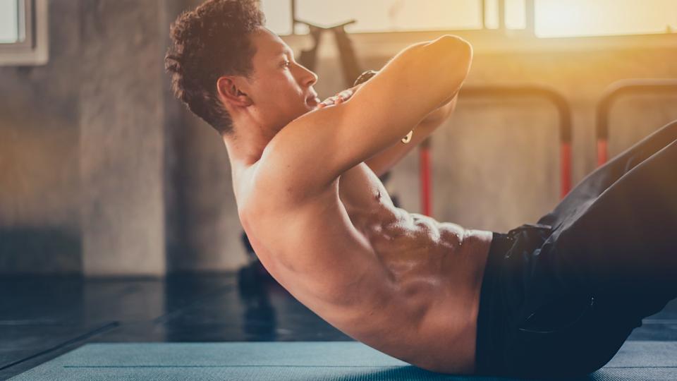 Male training topless during ab workout with hands on his shoulders laying down
