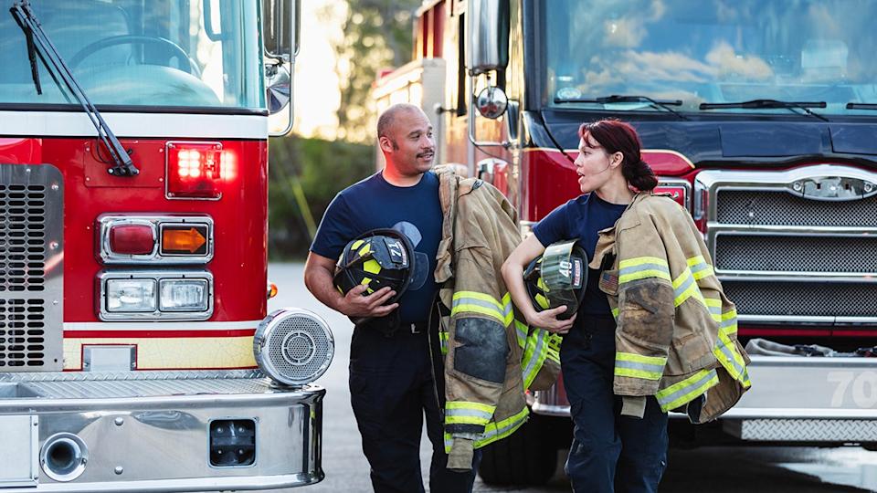 male and female firefighters talk while holding their gear